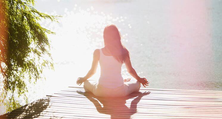 Woman meditating on a dock overlooking water.